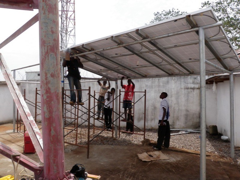 Team installing an elevated solar panel canopy beside a radio mast